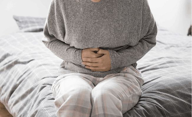 Close-up of person sitting in bed holding stomach with both hands