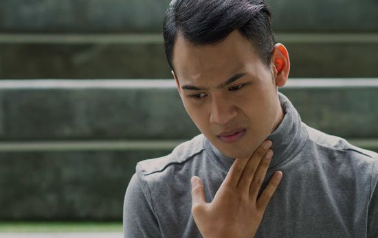 Person touching their throat, looking concerned. 