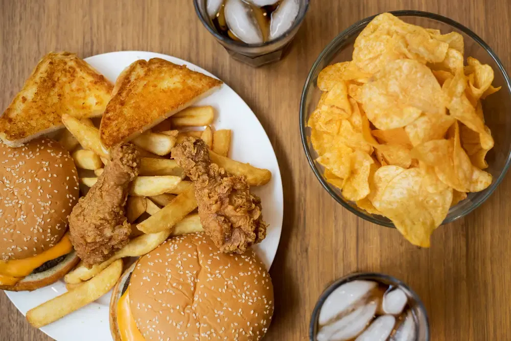 Various fast foods and soft drinks on wooden table