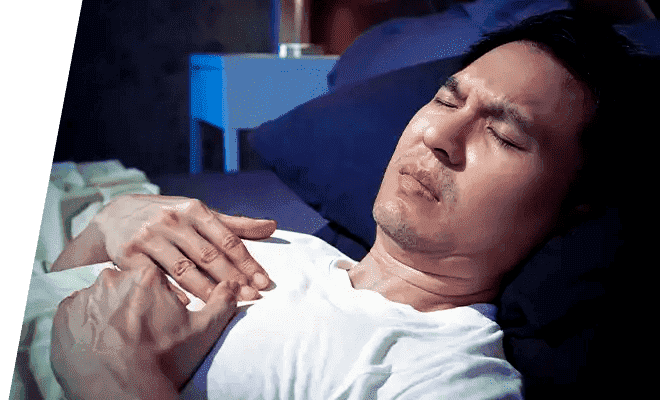 Man in bed with hands on chest experiencing acid reflux