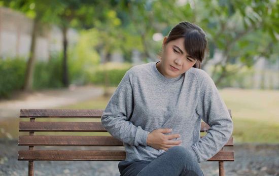 Woman sitting on a bench, holding her stomach in discomfort.
