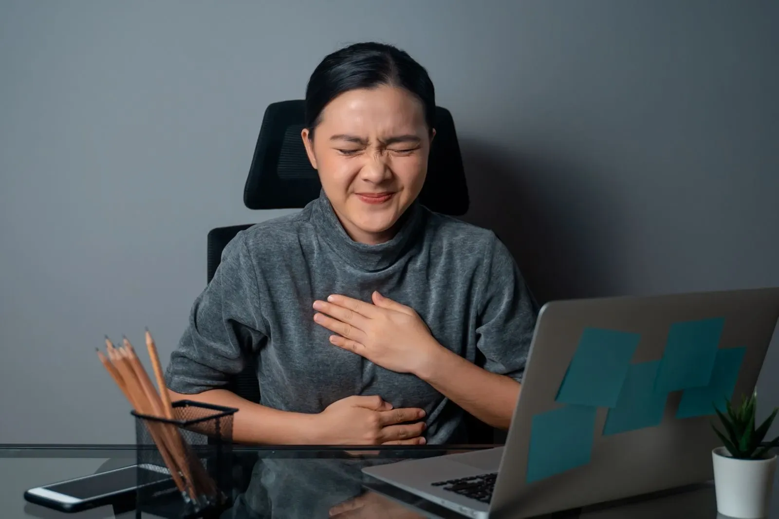 Woman in desk feeling acid reflux while working